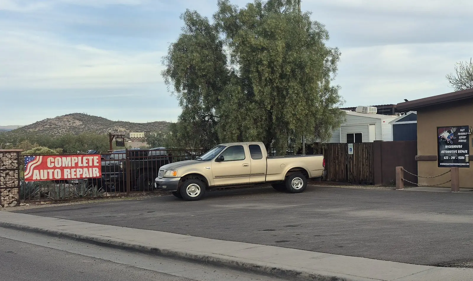 Wickenburg Automotive Repair on S Washington Street, with the red Complete Auto Repair banner on the fence and the desert hills behind